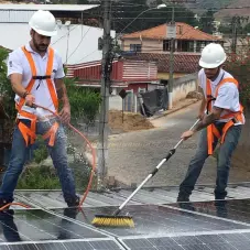 Dois colaboradores ativa lavando painéis fotovoltaicos com uma mangueira de água e vassoura
